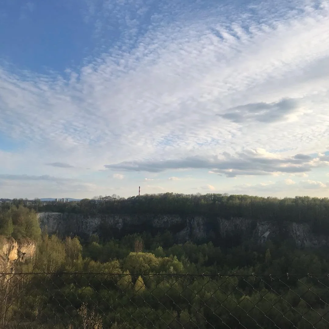 Scenic view of a cloudy sky above a green forested landscape with cliffs and a fence in the foreground.