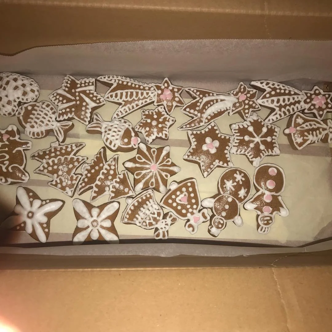 Decorated Christmas cookies inside a cardboard box, shaped like stars, snowflakes, ornaments, and flowers with white and pink icing.