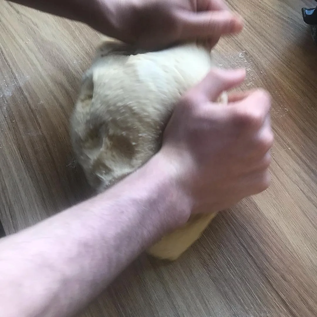 Person kneading dough on a wooden surface with a hand on top and a rabbit lying down adjacent.