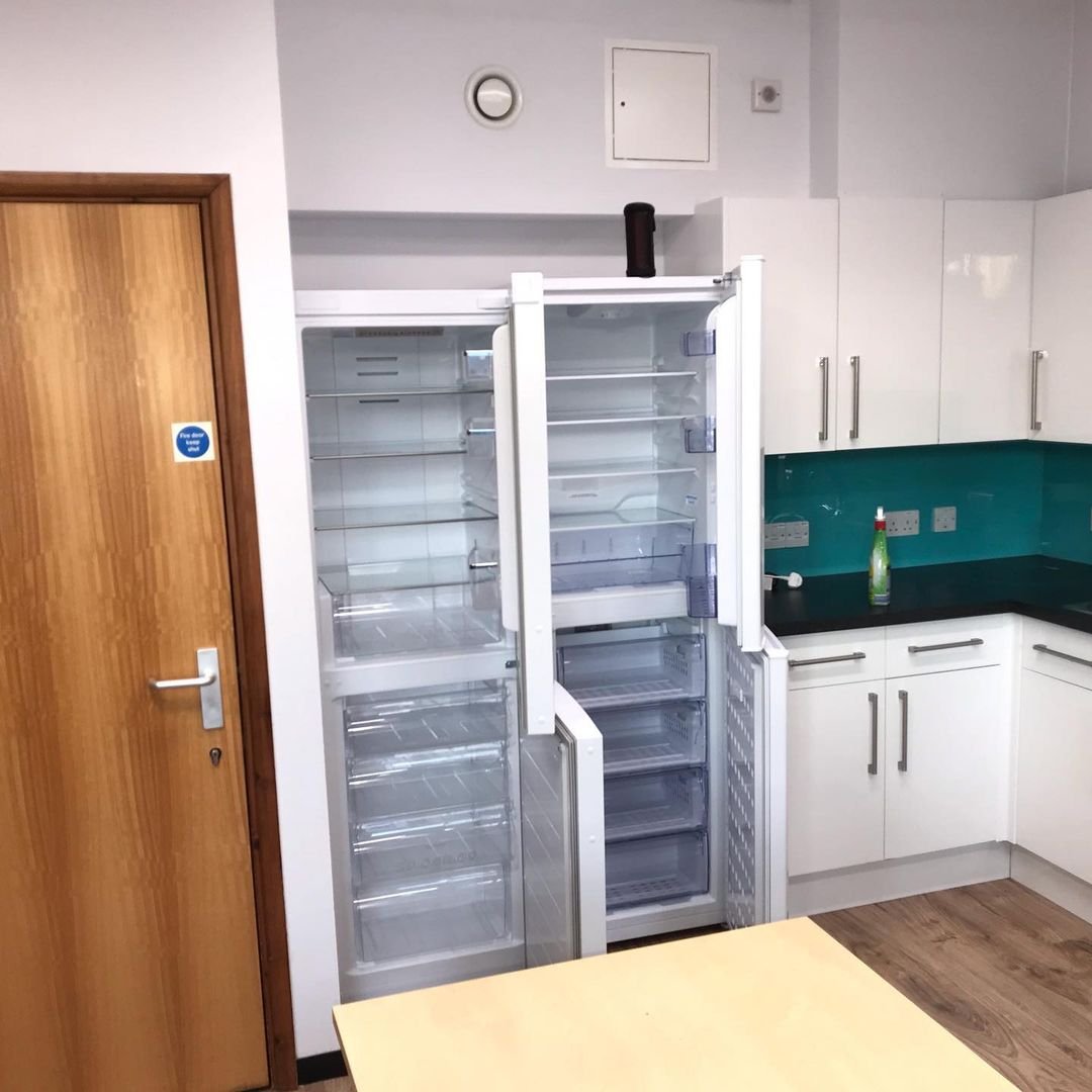 Empty commercial kitchen with open tall refrigerators, white cabinets, a green countertop, a soap dispenser, and a wooden door.