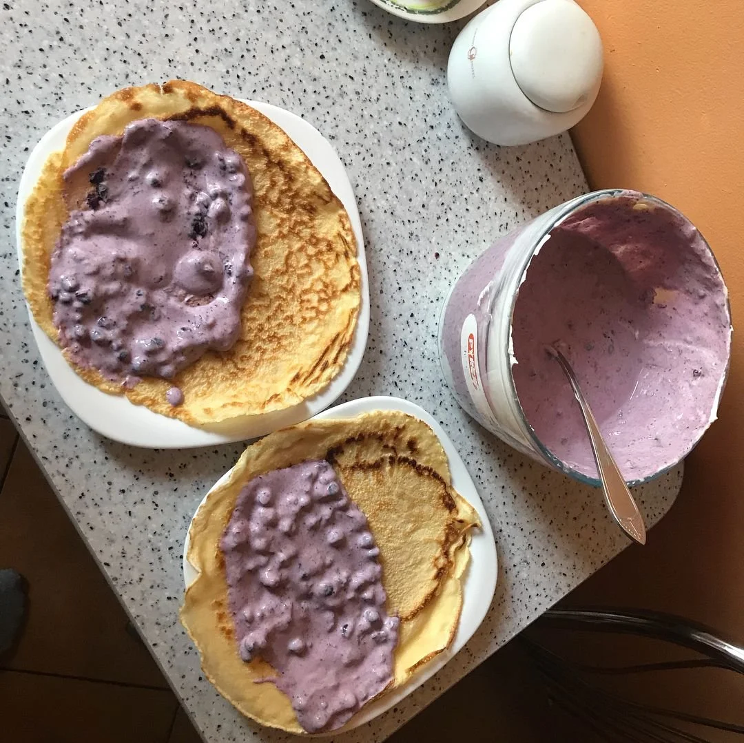 Two plates of crepes with blueberry whipped cream topping, a container of more whipped cream, and a salt shaker on a speckled countertop.