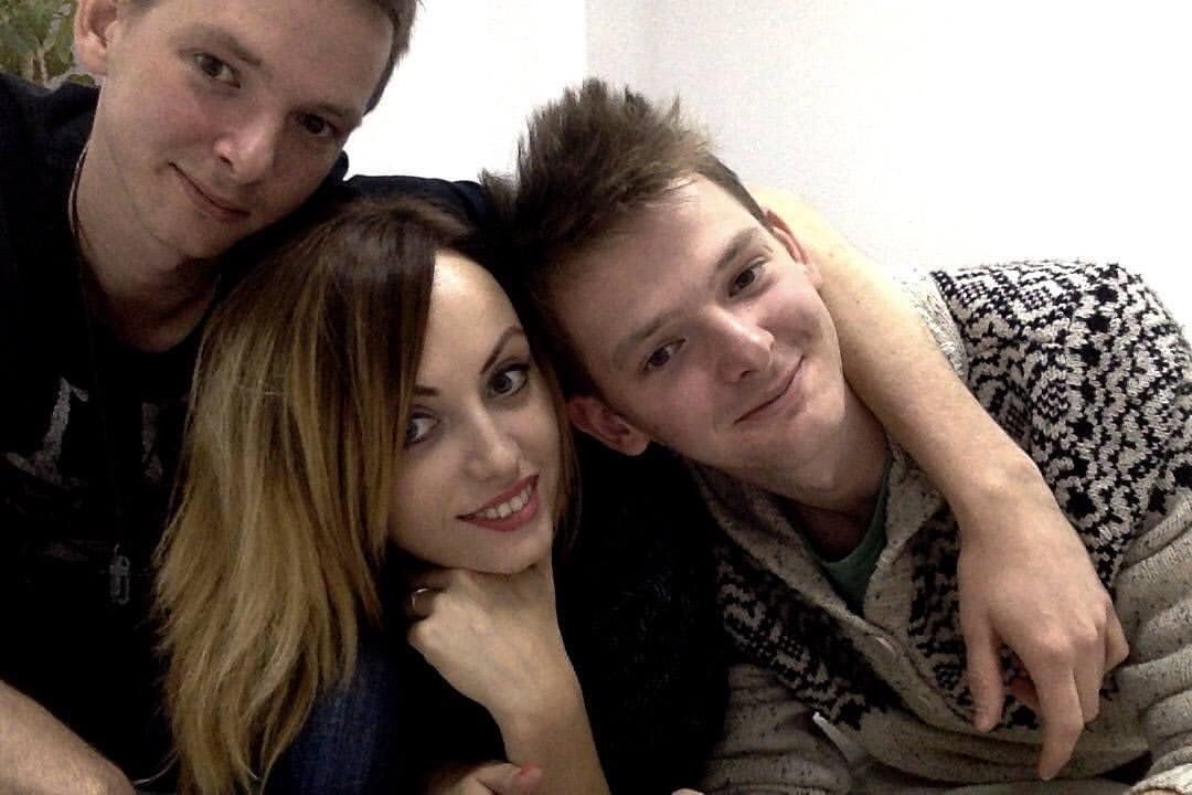 Three friends, two men and one woman, closely gathered indoors for a selfie, smiling at the camera.