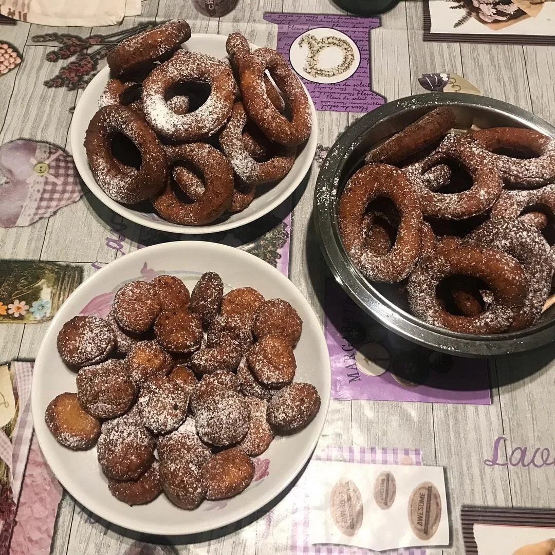Three dishes of fried dough snacks dusted with powdered sugar on a table.