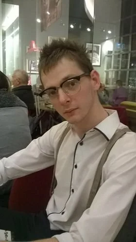 A young man wearing glasses and a white button-up shirt sitting at a table in a restaurant.