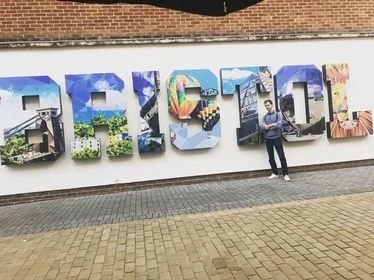 Person standing next to large, colorful block letters spelling 'TRICOR' on a white wall outside.