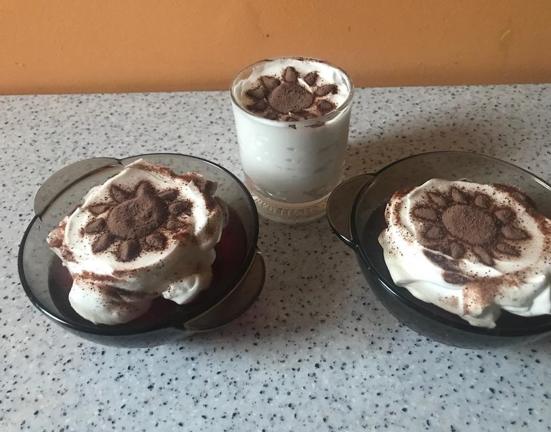 Three glasses with whipped cream and chocolate sprinkles on top, placed on a speckled gray countertop.