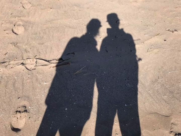 Shadows of two people on a sandy surface, facing each other.