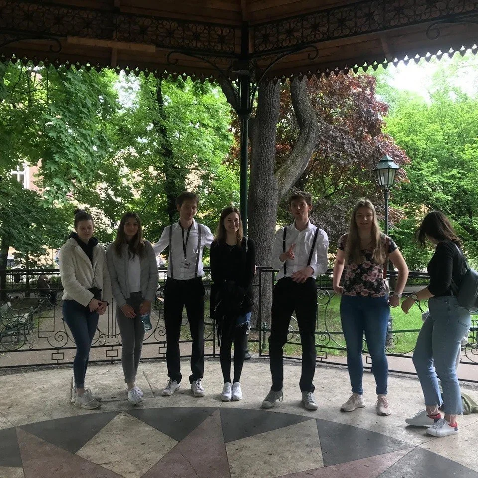Group of seven teenagers standing on a gazebo with green trees in the background, some holding water bottles, some with backpacks.