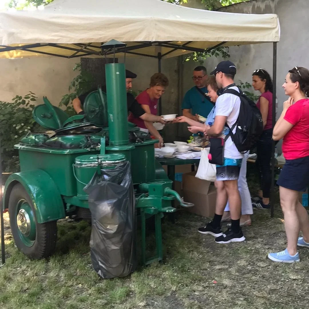 People standing in line at a food stand with a green mobile food cart, serving bowls of food outdoors under a canopy.