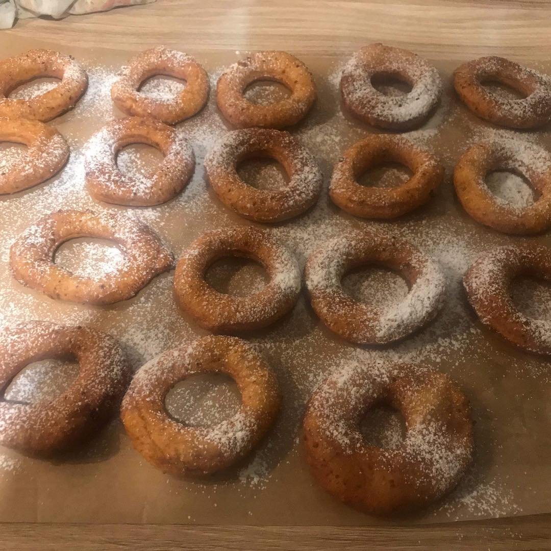 A tray of freshly baked donuts dusted with powdered sugar, arranged on parchment paper.