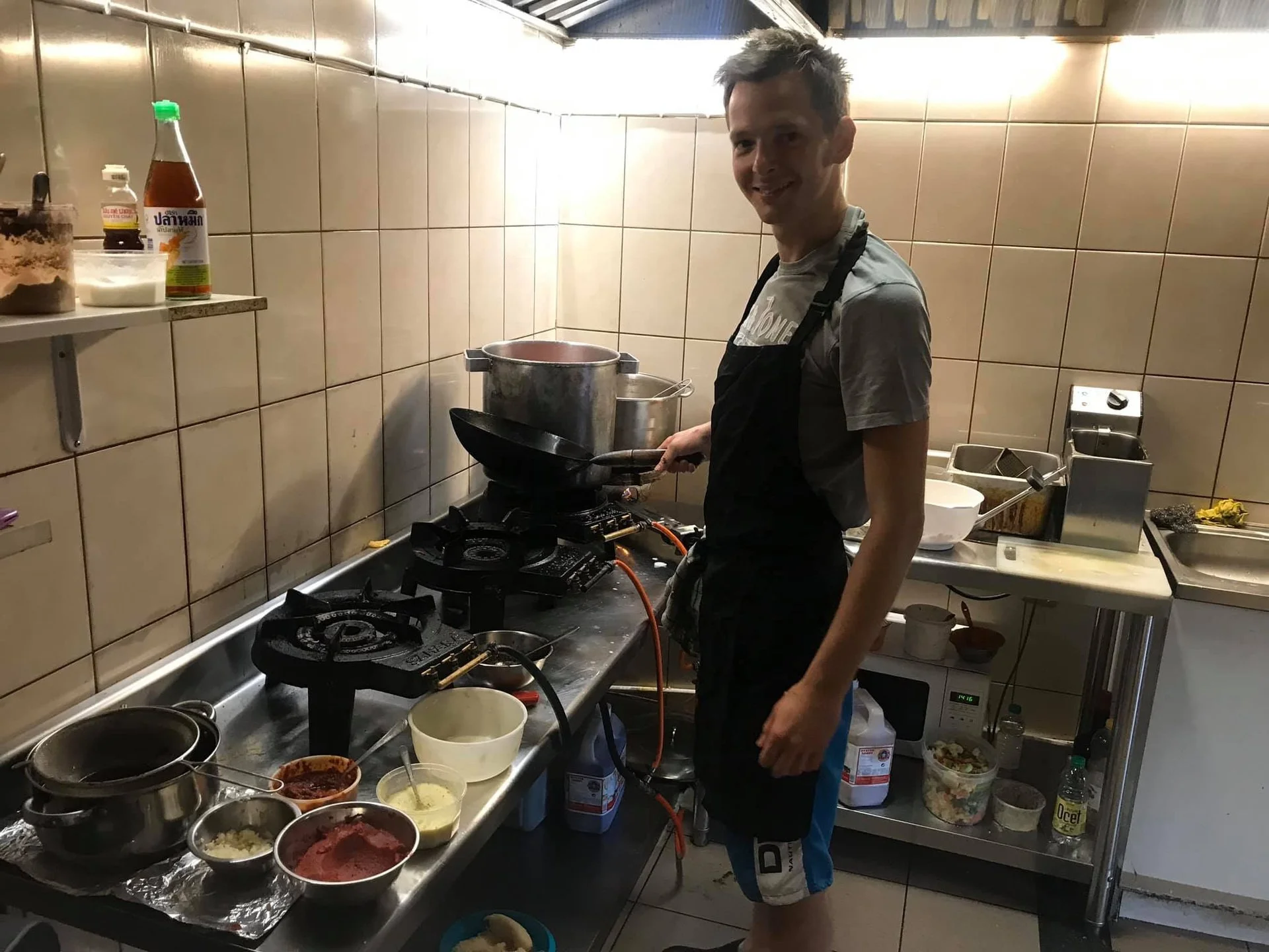 Man cooking in a small kitchen, standing at a stove with pots and ingredients on the counter.