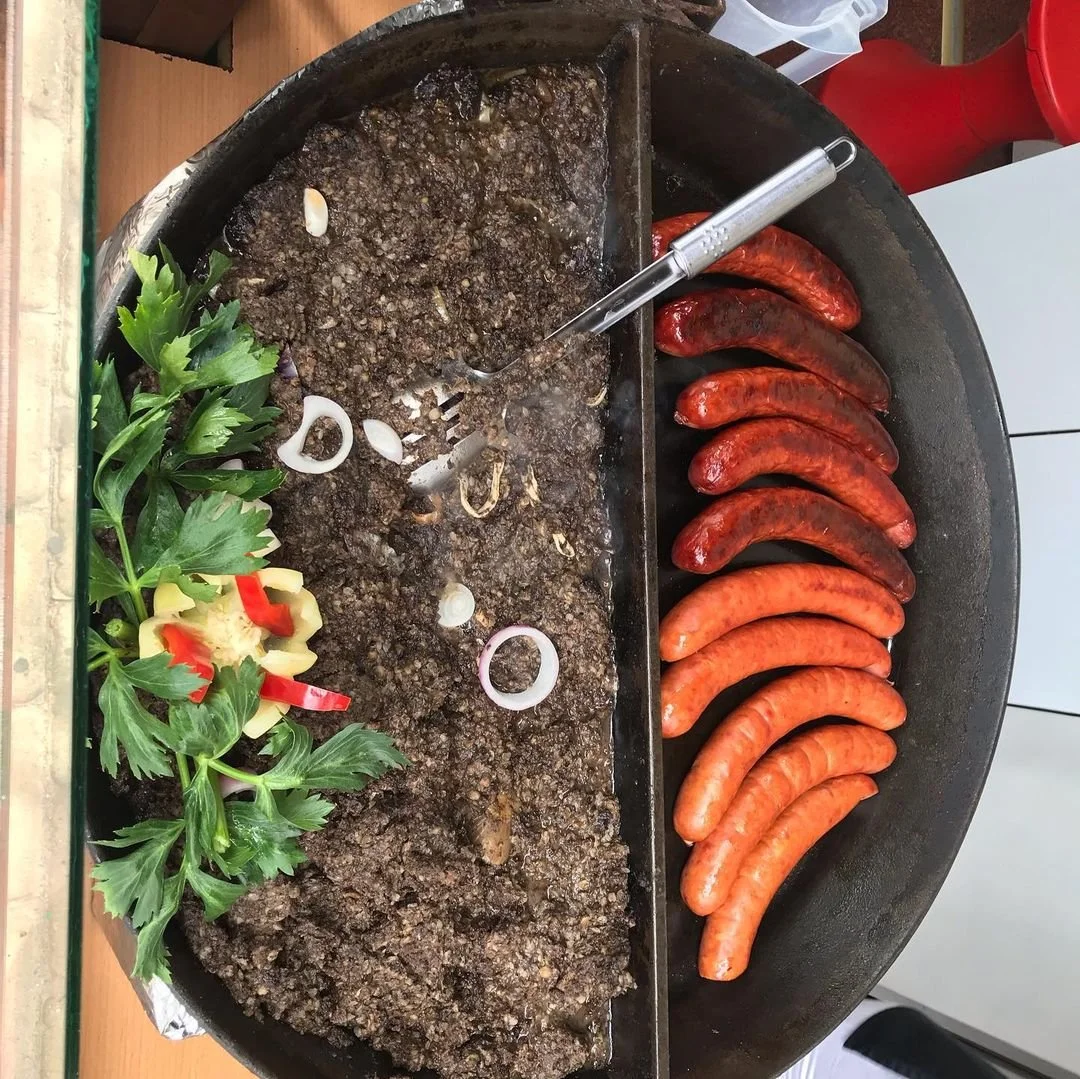 A large round grill divided into two sections with various cooked meats and vegetables. Left side shows cooked ground meat with chopped onions and parsley, right side has grilled sausages in different shades of red and orange.