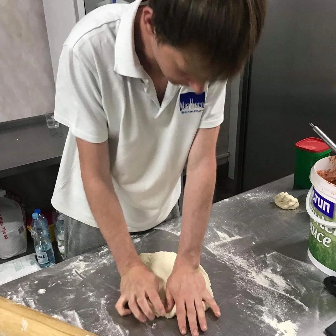 A person kneading dough on a floured table in a kitchen.