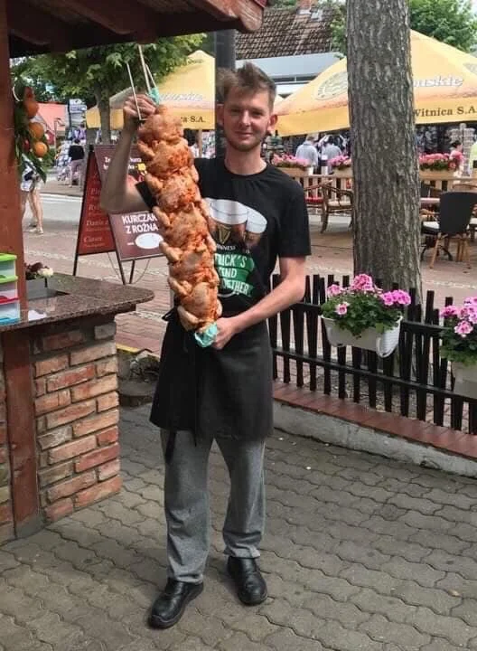 Young man holding large skewer of fried chicken at outdoor eatery.