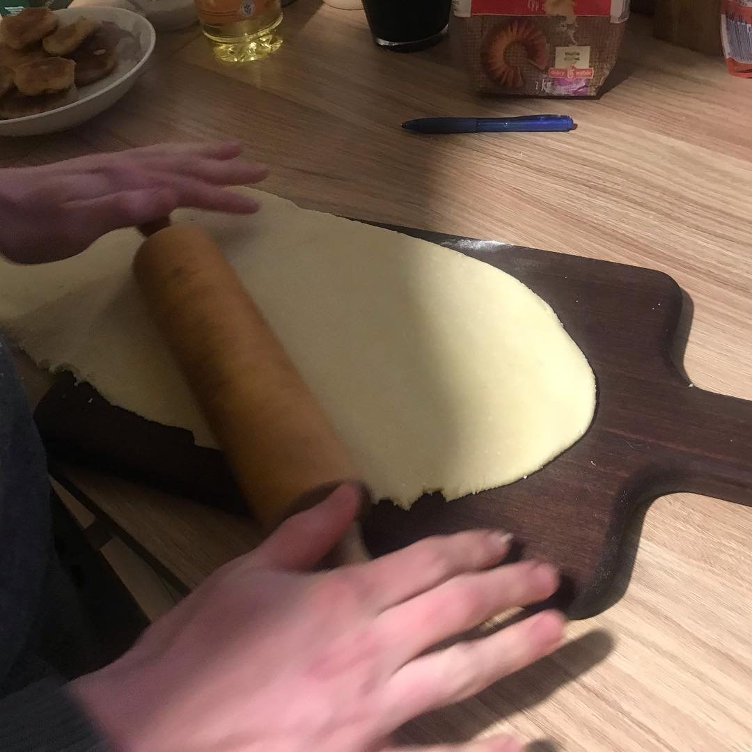 Person rolling out dough on a wooden board using a rolling pin.