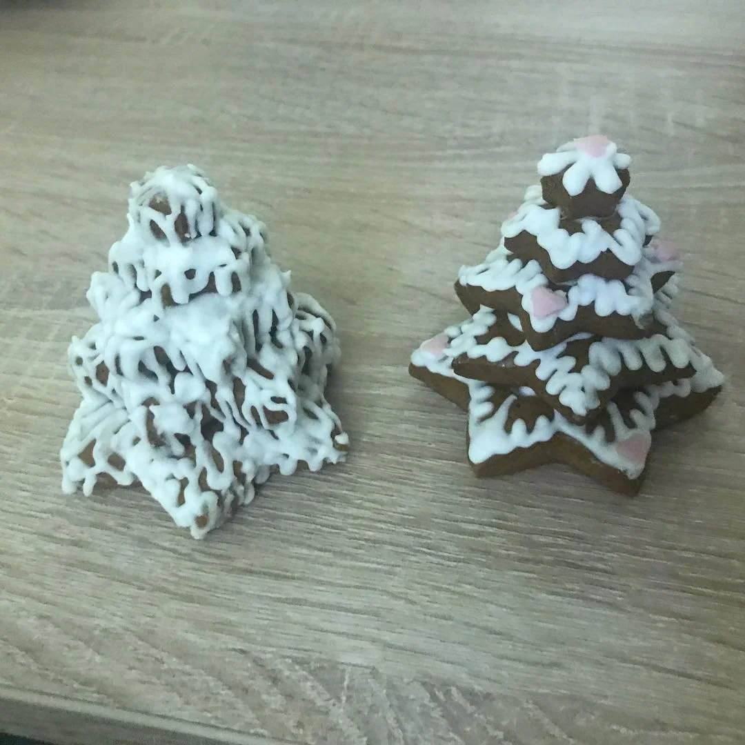 Two gingerbread cookies decorated as Christmas trees with white icing and pink accents, placed on a wooden surface.