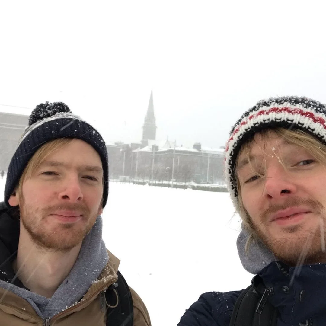 Two men taking a selfie in a snowy landscape with a church steeple in the foggy background.