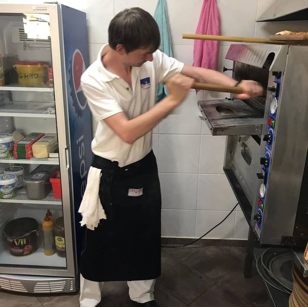 A pizza chef throwing dough into an oven in a kitchen.