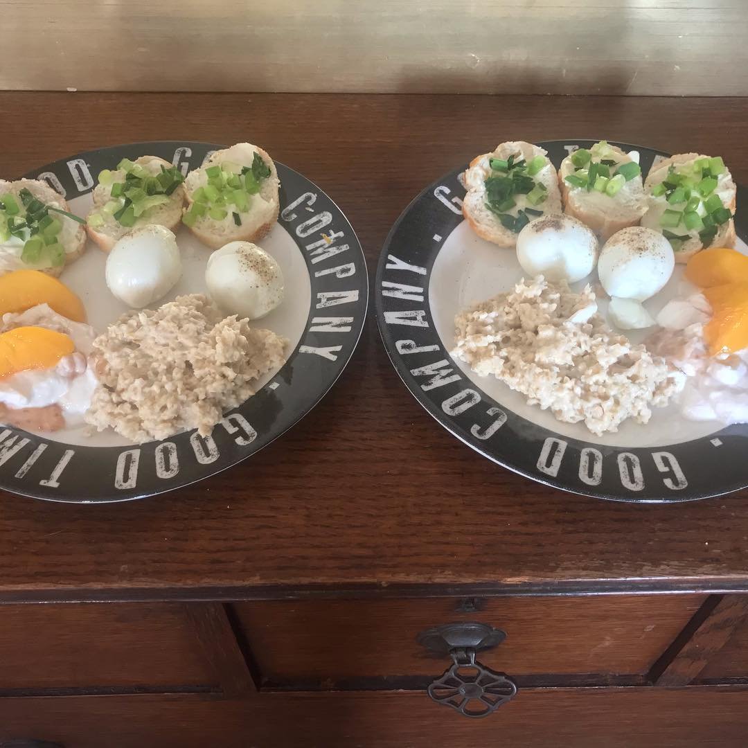 Two breakfast plates with fried eggs, potato hash, dinner rolls topped with chopped green onions, and dollops of sour cream served on black and white plates.