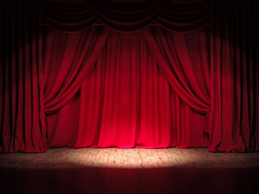 Red theater curtain closed on a wooden stage with spotlight on the center.