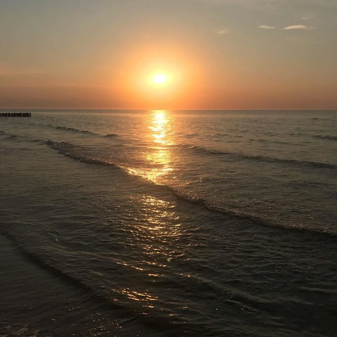 Sunset over the ocean with gentle waves and a reflection of the sun on the water.