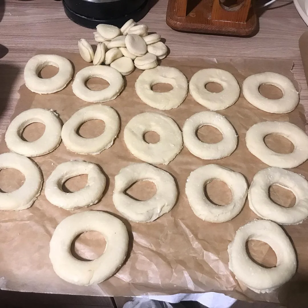 Unbaked donut rings and a pile of white chocolate chips on parchment paper on a wooden countertop.
