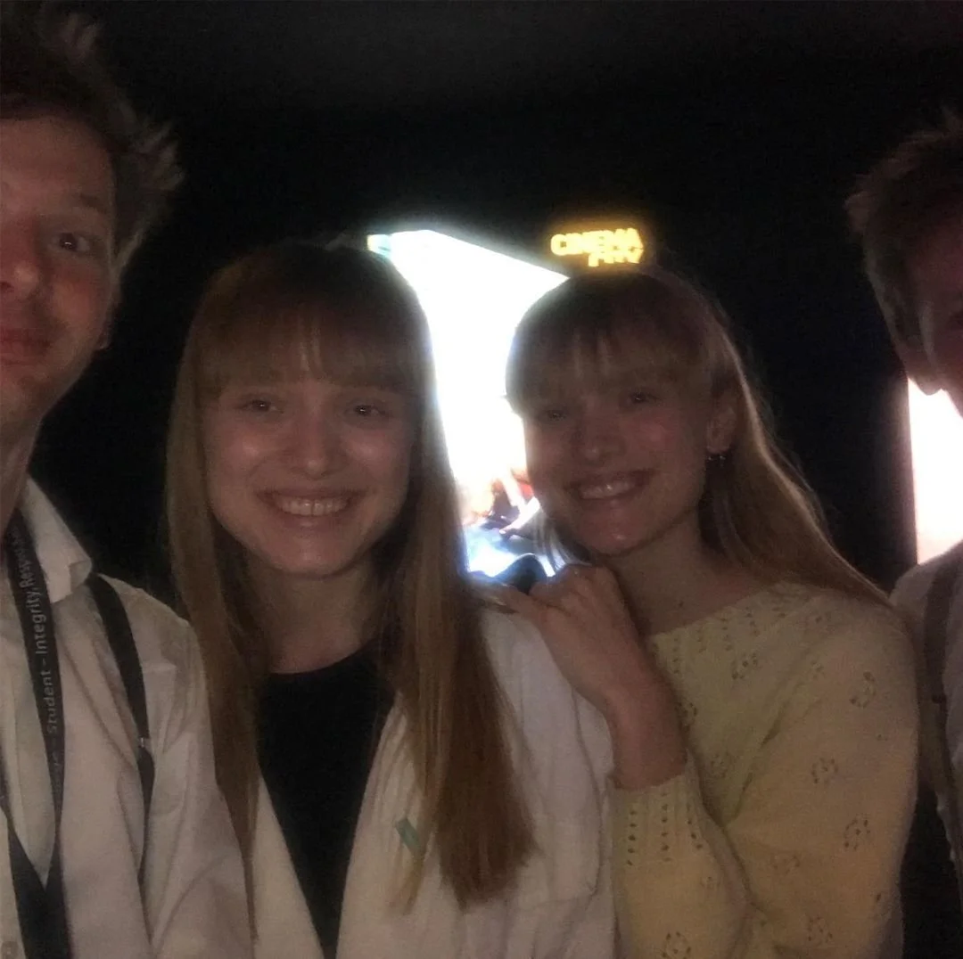 Four people smiling at the camera in a dark room with a bright opening behind them.