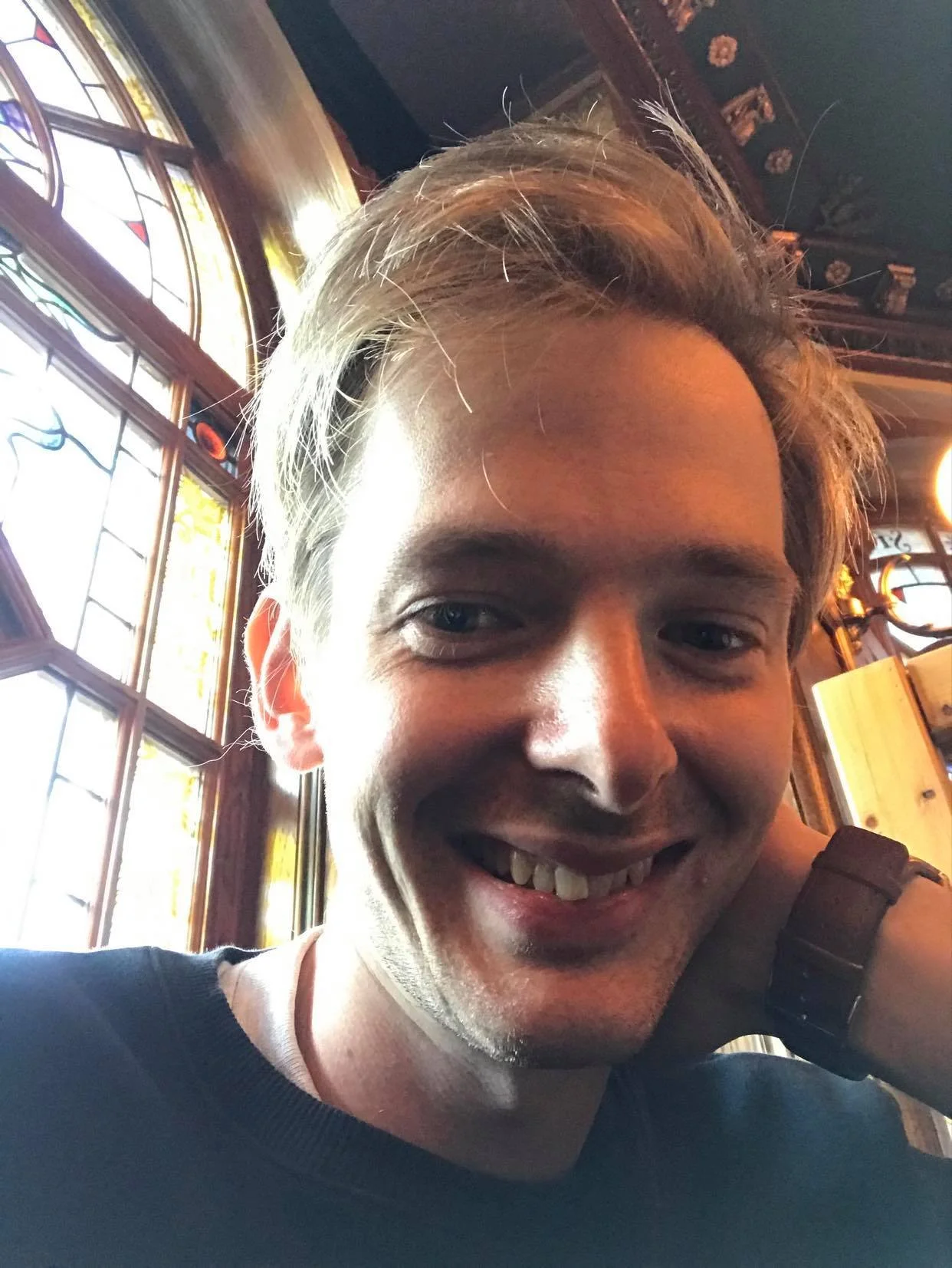 A young man smiling inside a room with stained glass windows and wooden decor.