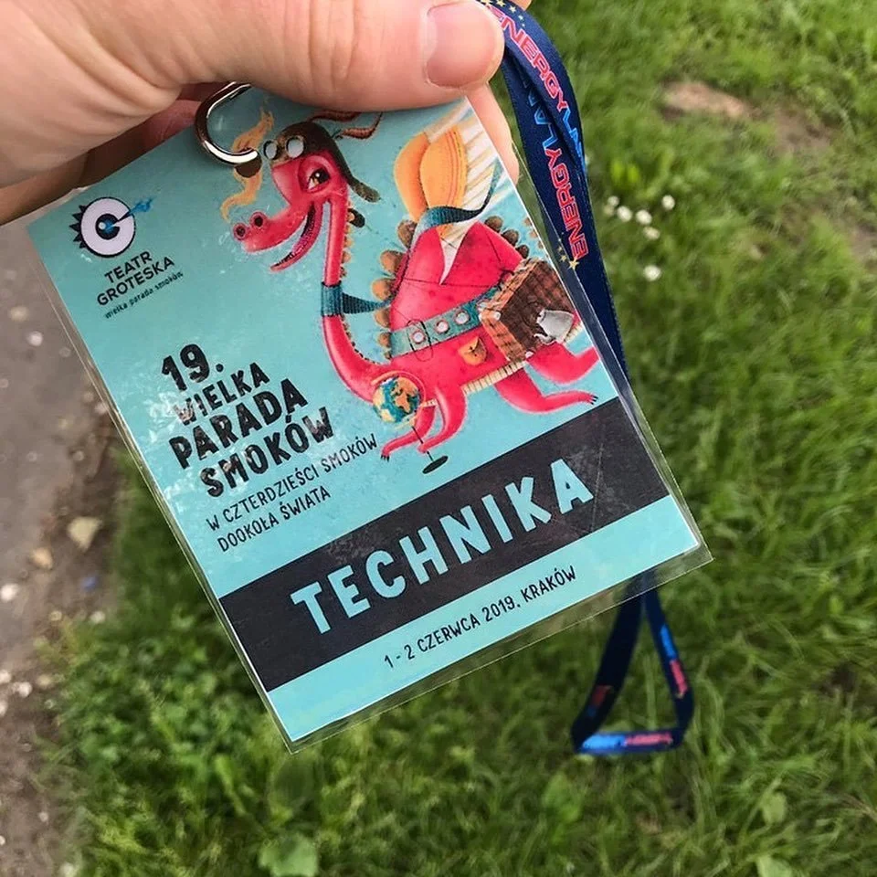 Colorful event badge featuring a cartoon dragon with pink body, rainbow hair, and blue glasses, holding a glass of drink, with text in Polish announcing the 19th Great Parade of Smokies in Krakow on June 1-2, 2019, at the Technical school.