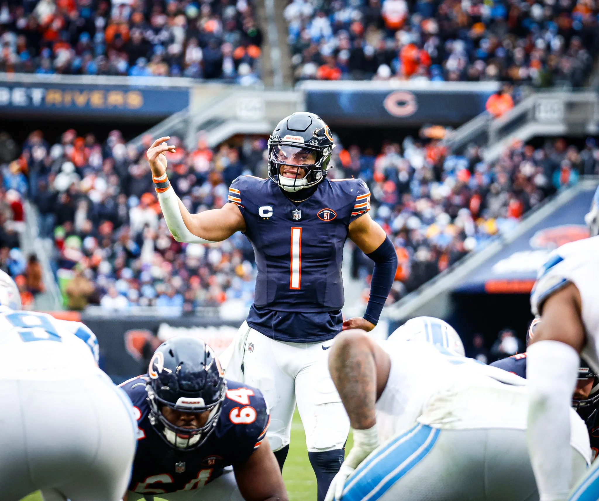 Chicago Bears football player standing with a raised arm on the field during a game with other players and a crowd in the background.