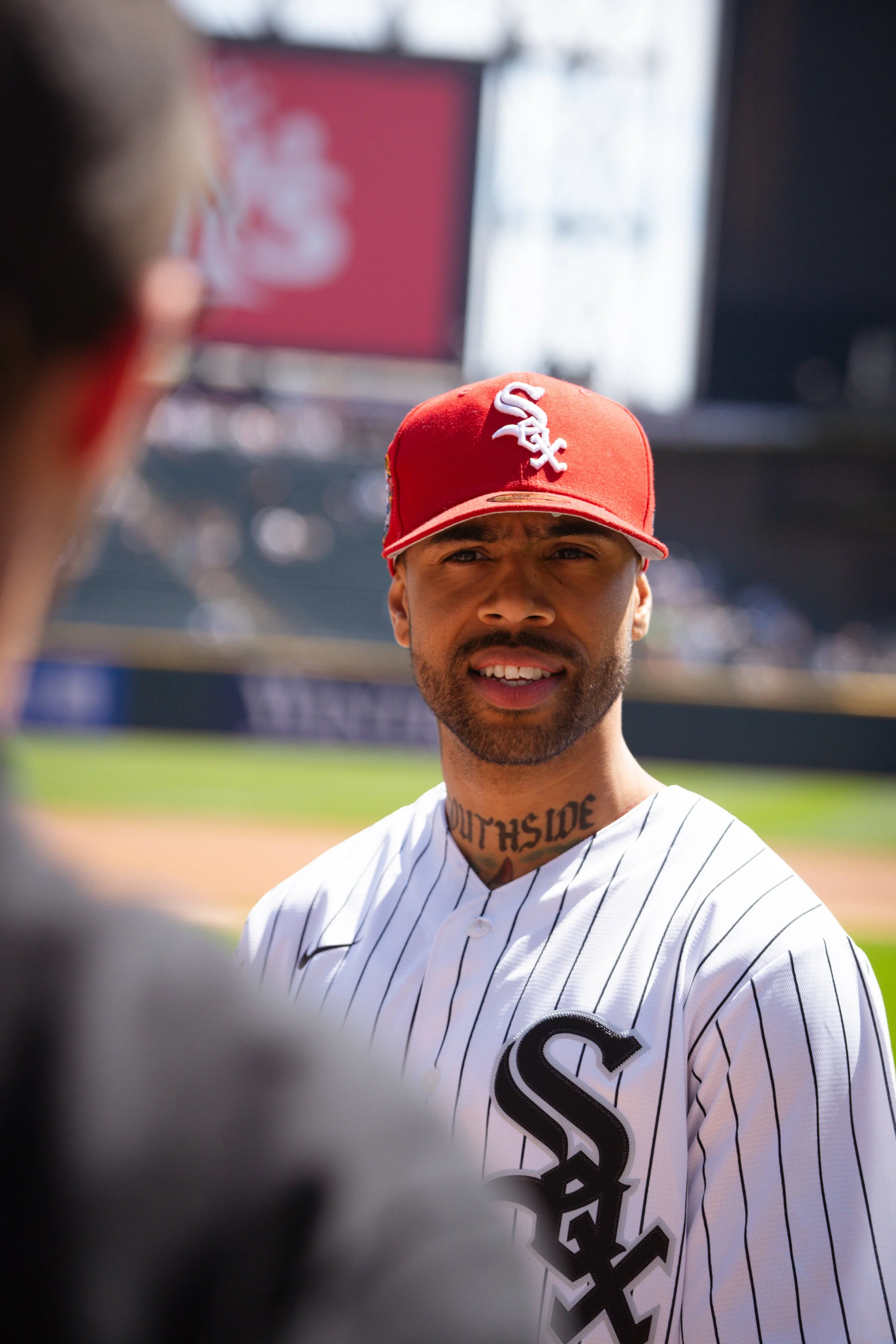 A baseball player wearing a white pinstripe uniform and a red cap with the Chicago White Sox logo, standing on the field during a game.