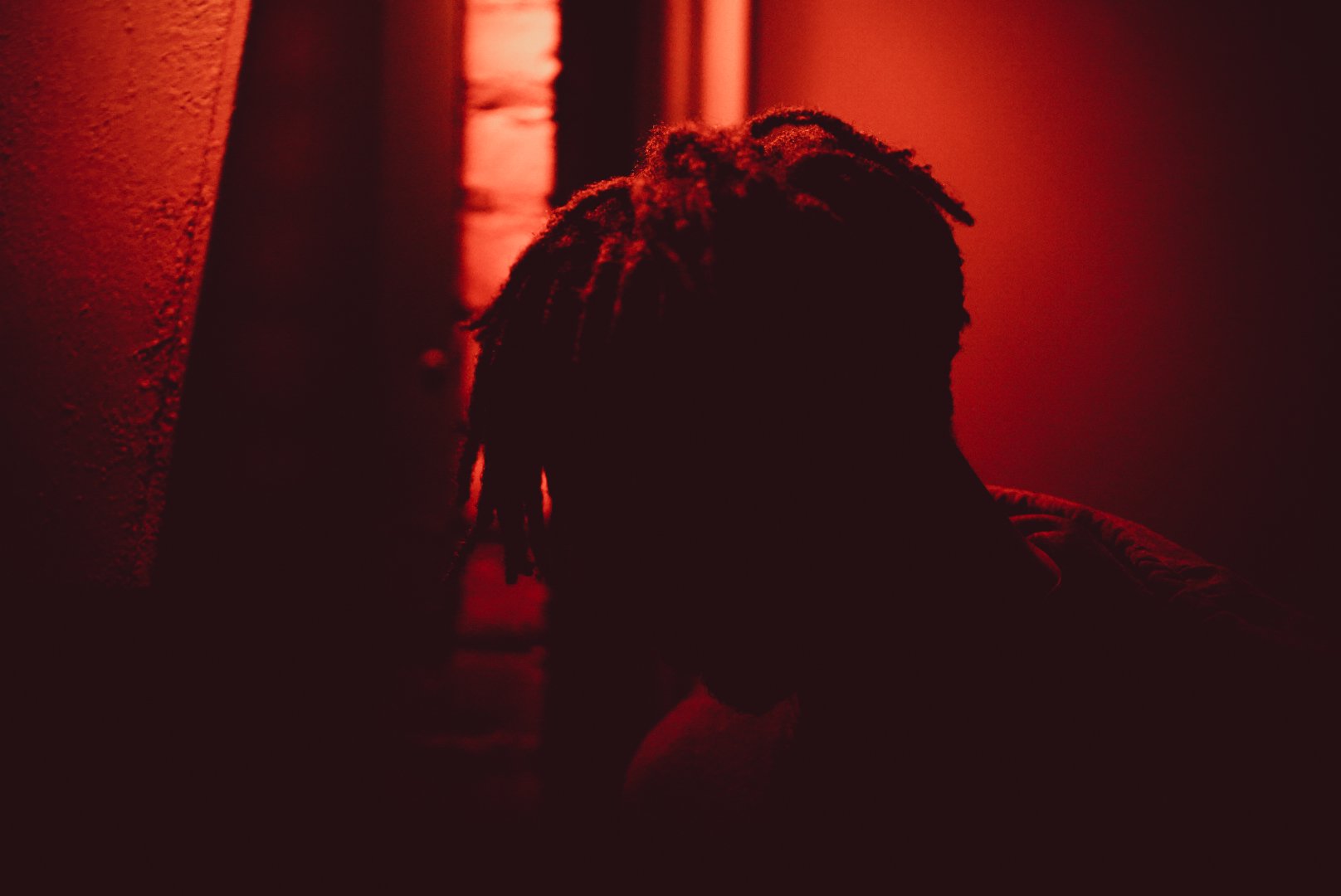 Silhouette of a person with dreadlocks against a red-lit background.