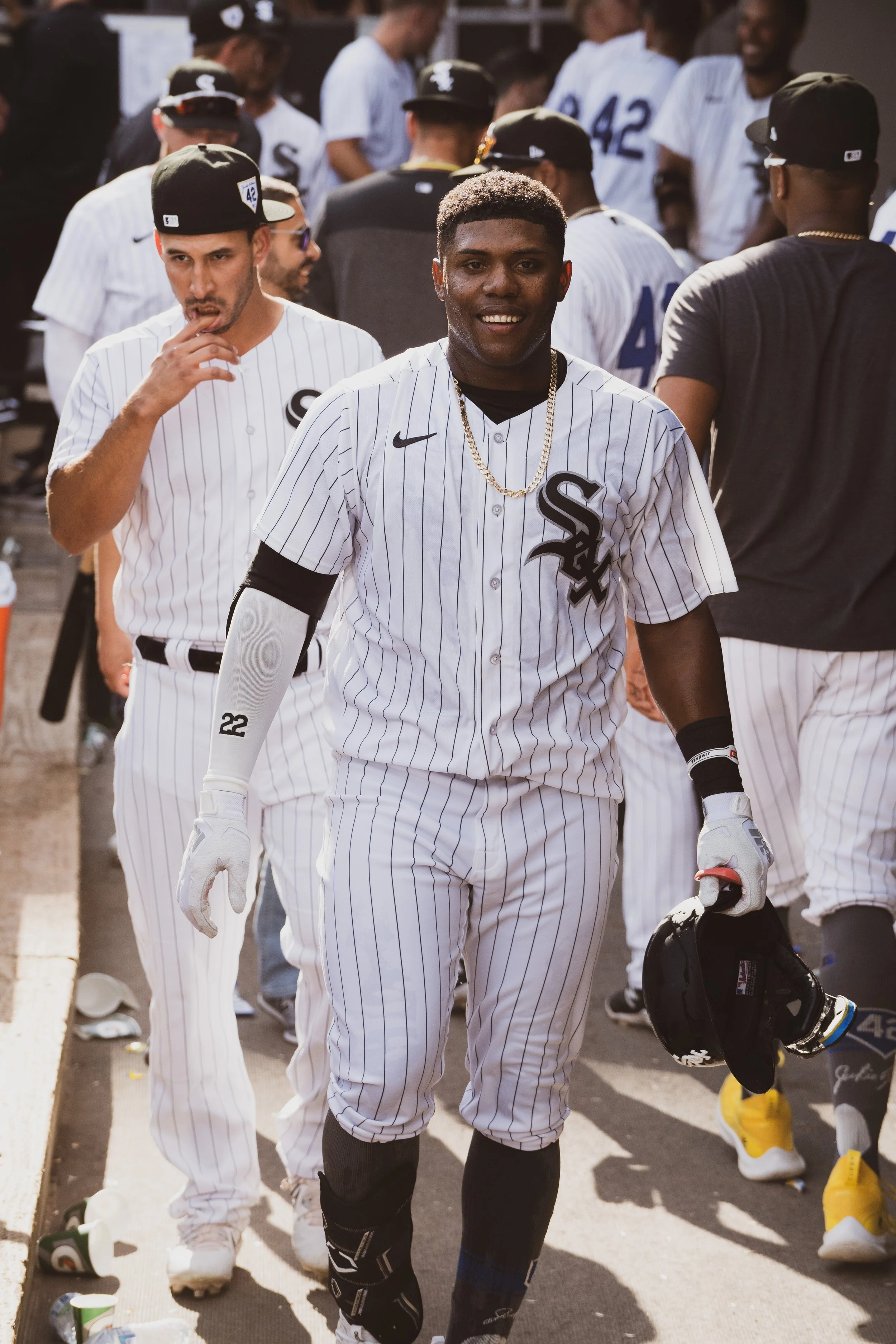 A group of baseball players in white pinstriped uniforms with the Chicago White Sox logo, some wearing black caps, standing and walking on a baseball field, holding helmets and gear.