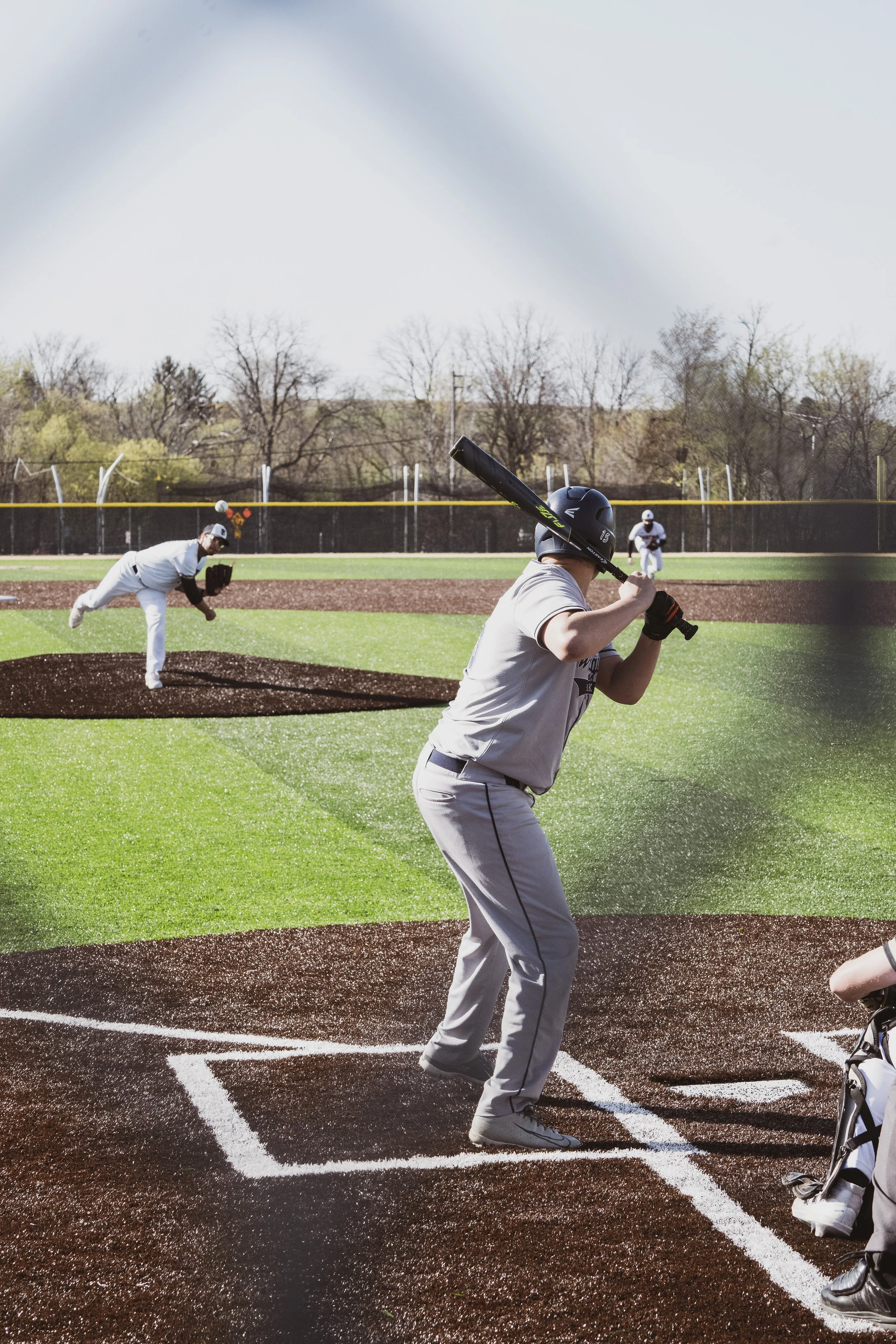 A baseball player stands at home plate ready to hit during a game, with other players visible in the background on the field.