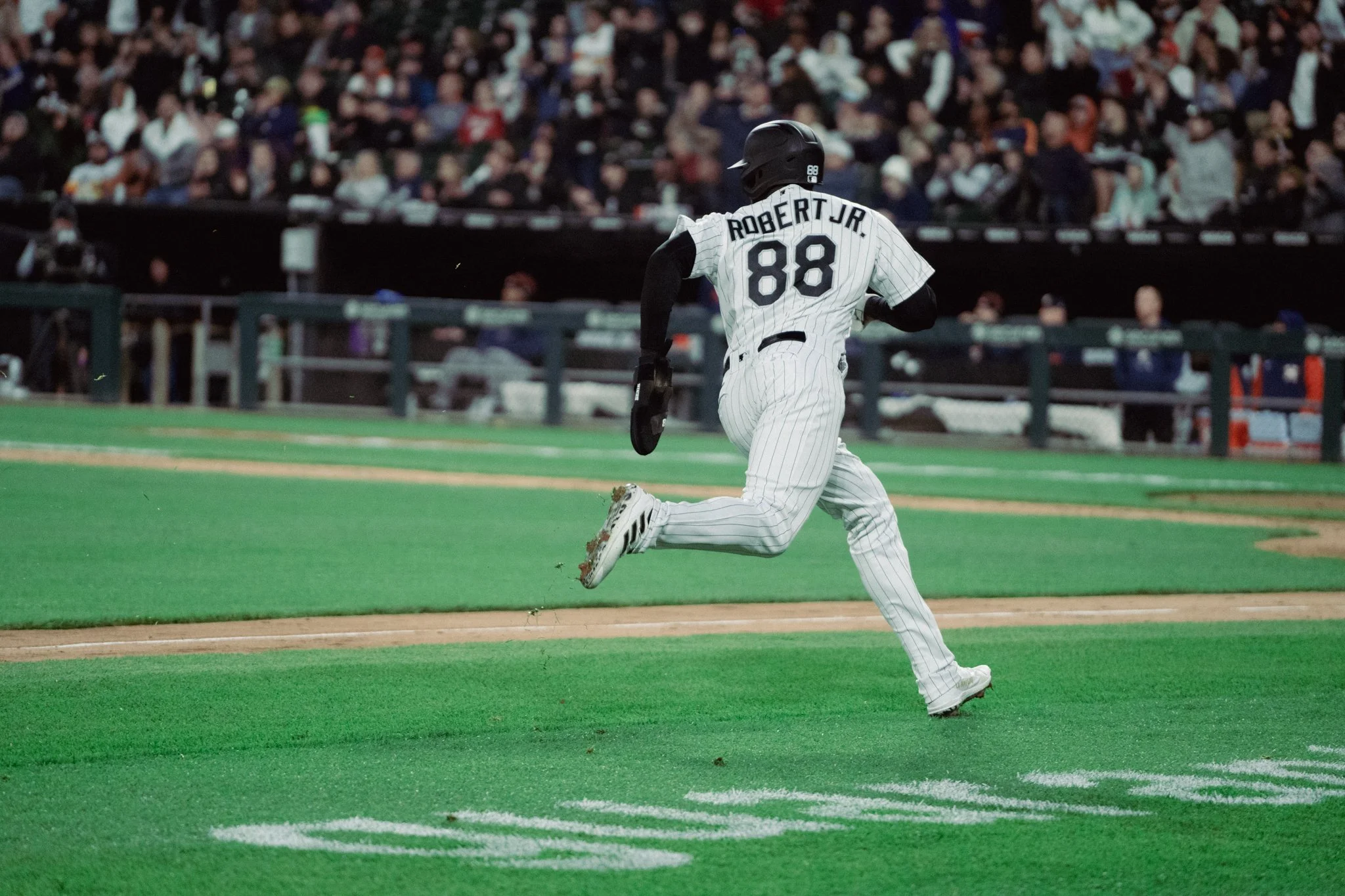 A baseball player wearing a pinstripe uniform with the name Robert Jr. and number 88, running on the field toward home plate at night, with a crowd in the stands in the background.
