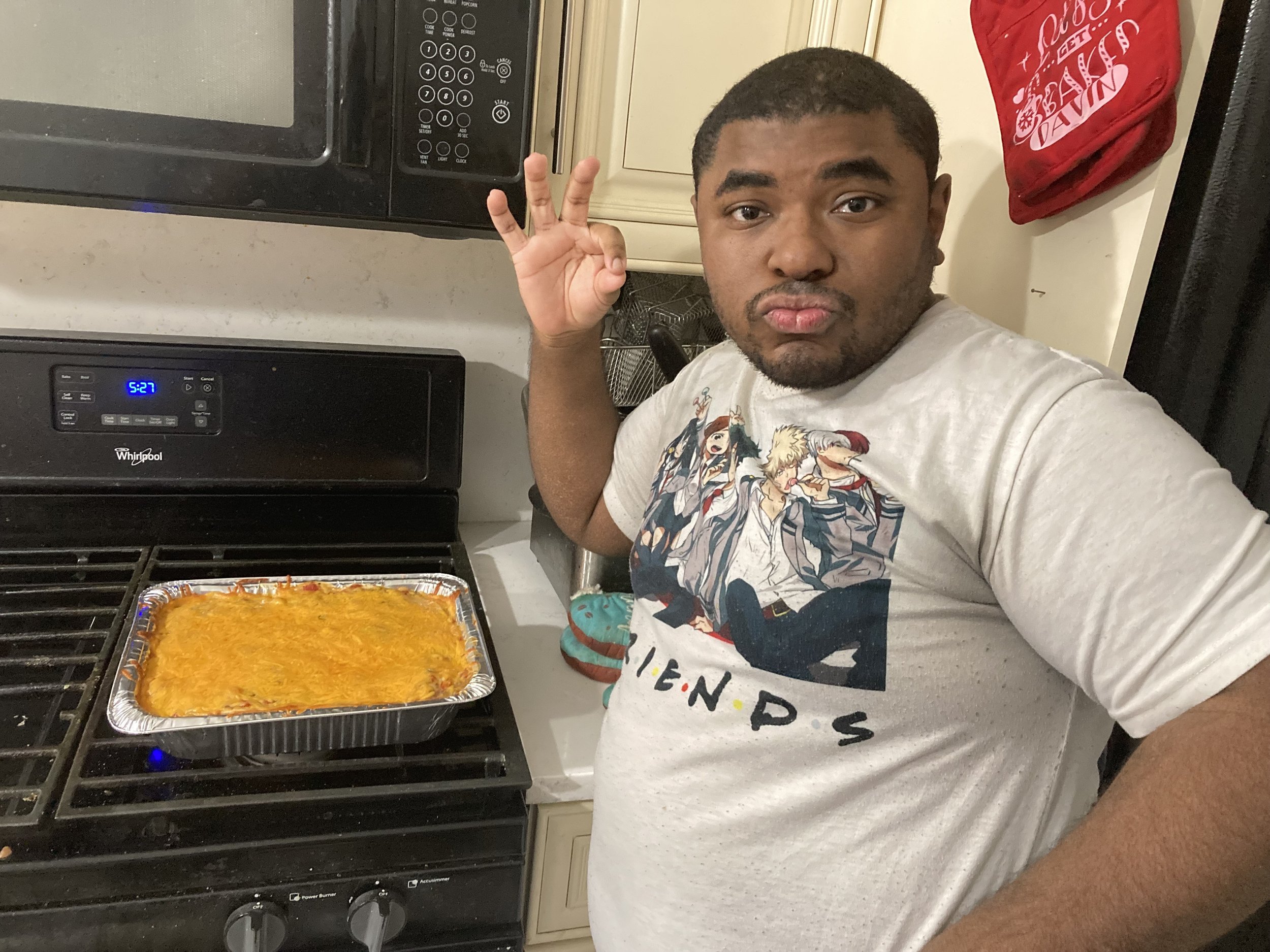 David makes the "chef's kiss" symbol with his fingers while posing for the camera in his kitchen.  Beside him is a freshly baked casserole.