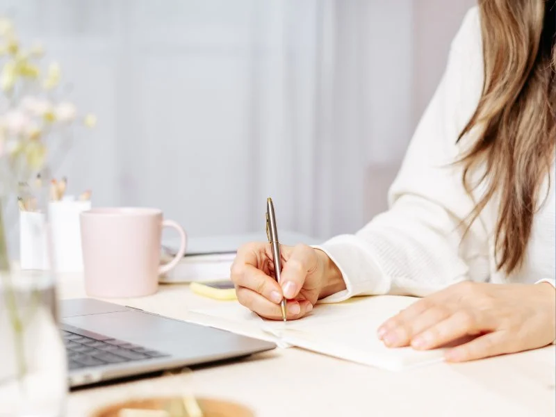 Writing notes at desk with laptop