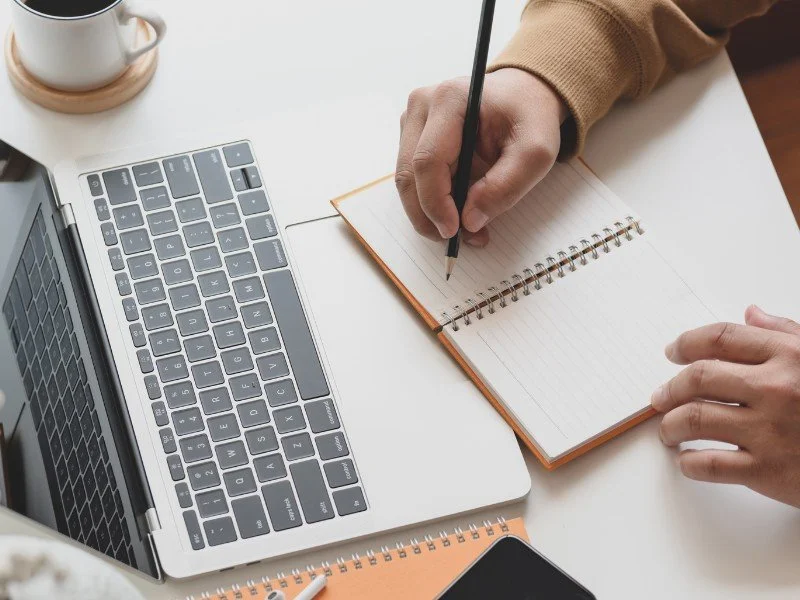 Writing and planning on a notebook with a laptop.