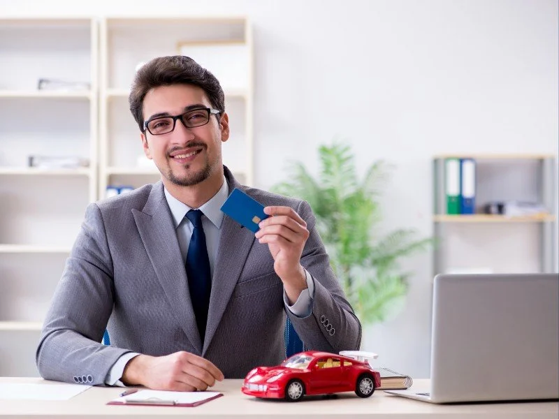 Friendly car salesman holding key card.