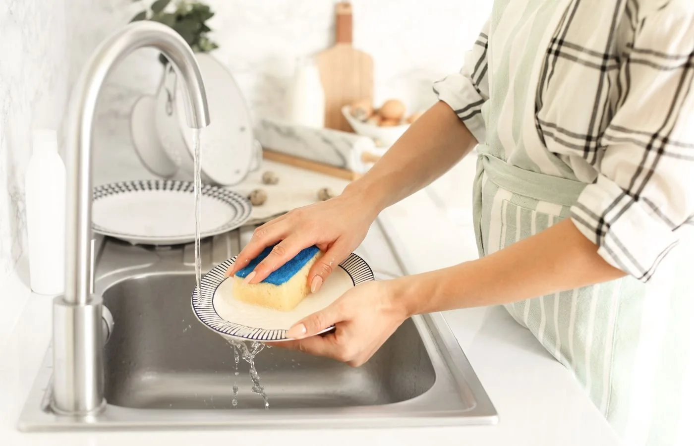 Person cleaning a plate in a kitchen sink