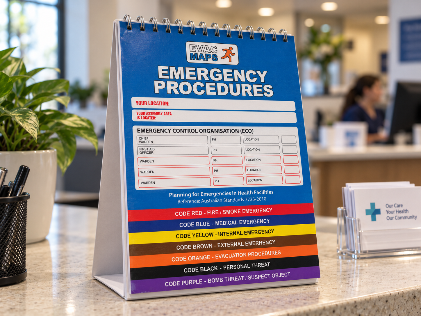 A sign displaying emergency procedures, with sections for location details and contact information, organized by color codes indicating different emergency types, placed on a table in a healthcare facility.
