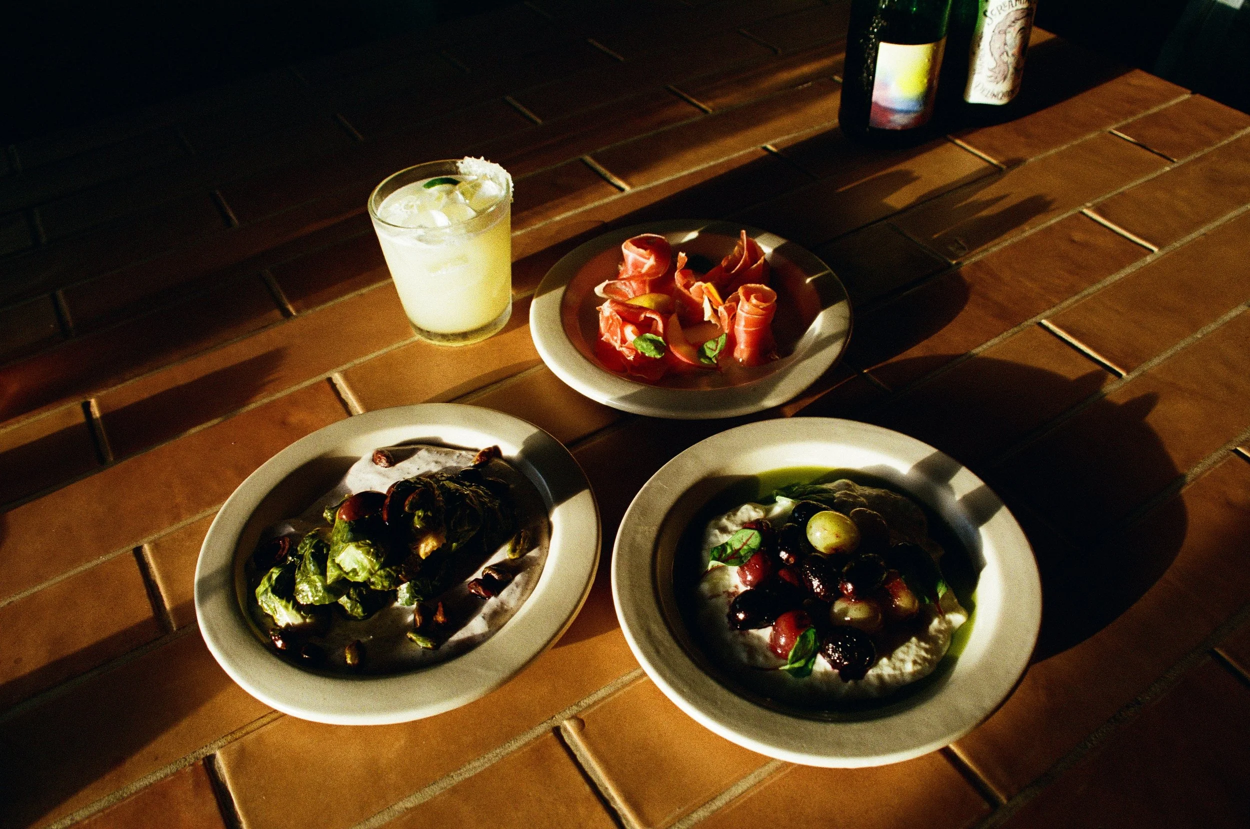 Three plates of food with a drink on a wooden table in a dimly lit setting.  Gold Coast restaurant food photography 