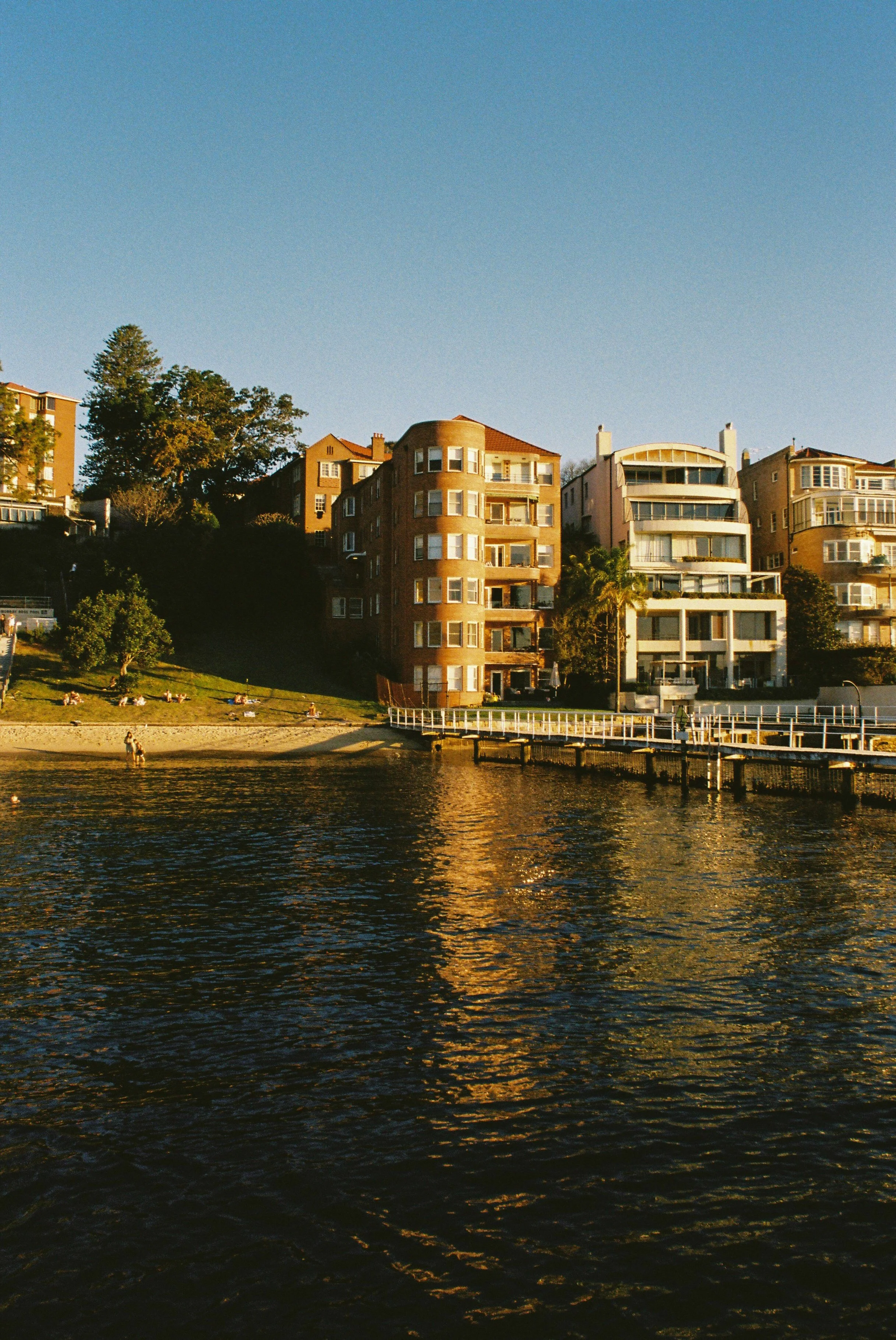 Riverside houses and apartments on a hillside during sunset, with the river in the foreground and a clear blue sky above. Garron Tower Art Deco architecture