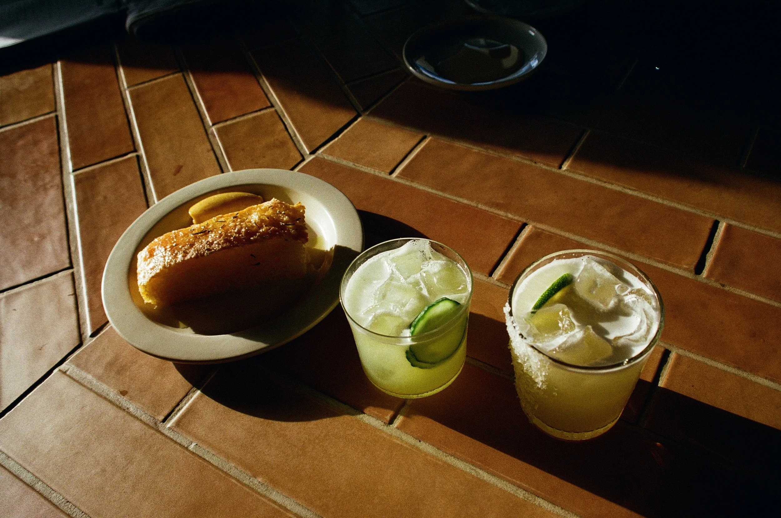 A slice of pie on a white plate with lemon slices, two glasses of margarita with salt on the rim and lime wedges, on a tiled surface.  Gold Coast restaurant marketing 