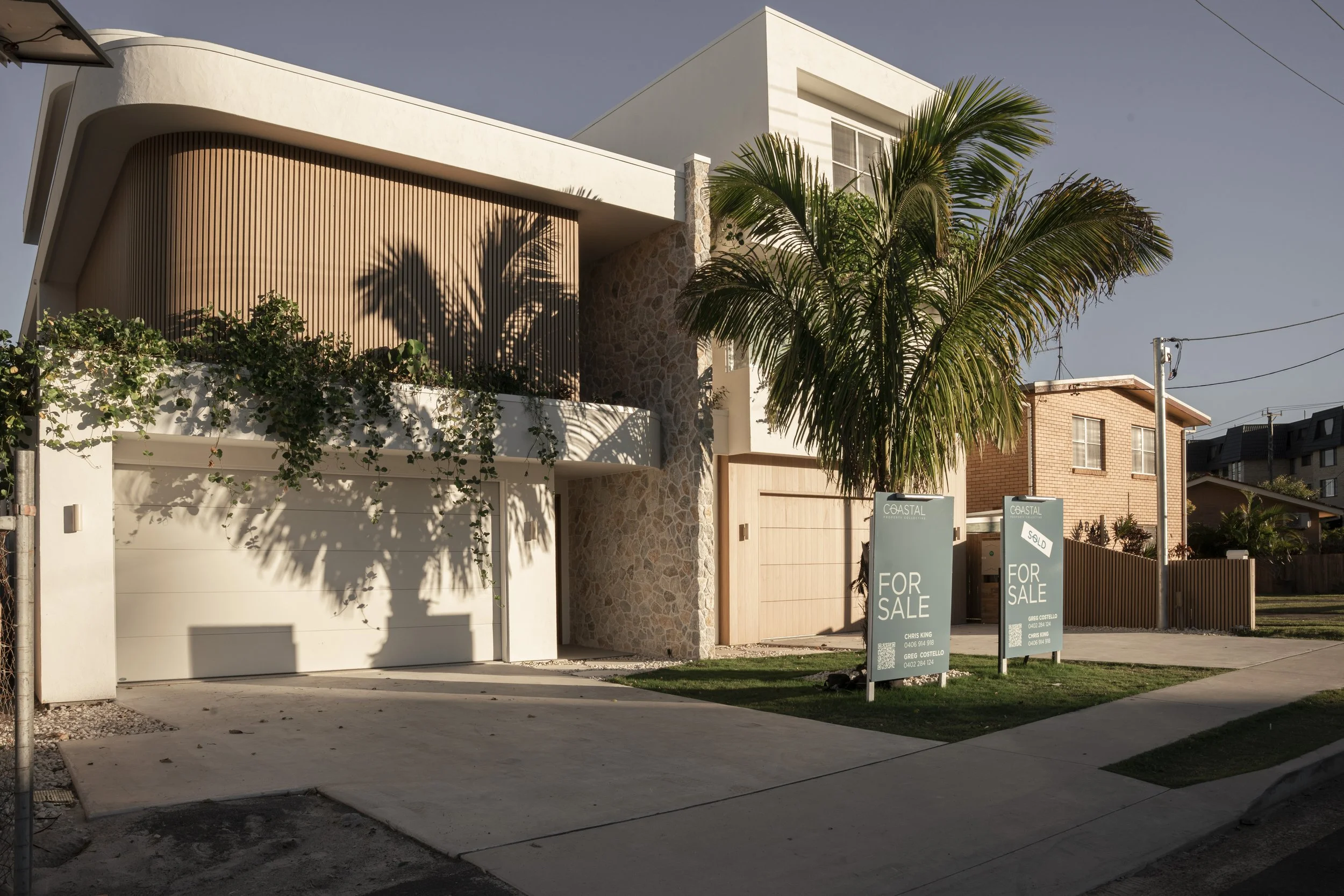Modern two-story house for sale with a palm tree in front and signs indicating it is sold and for sale. Architectural photography by Joey Bailey, Gold Coast