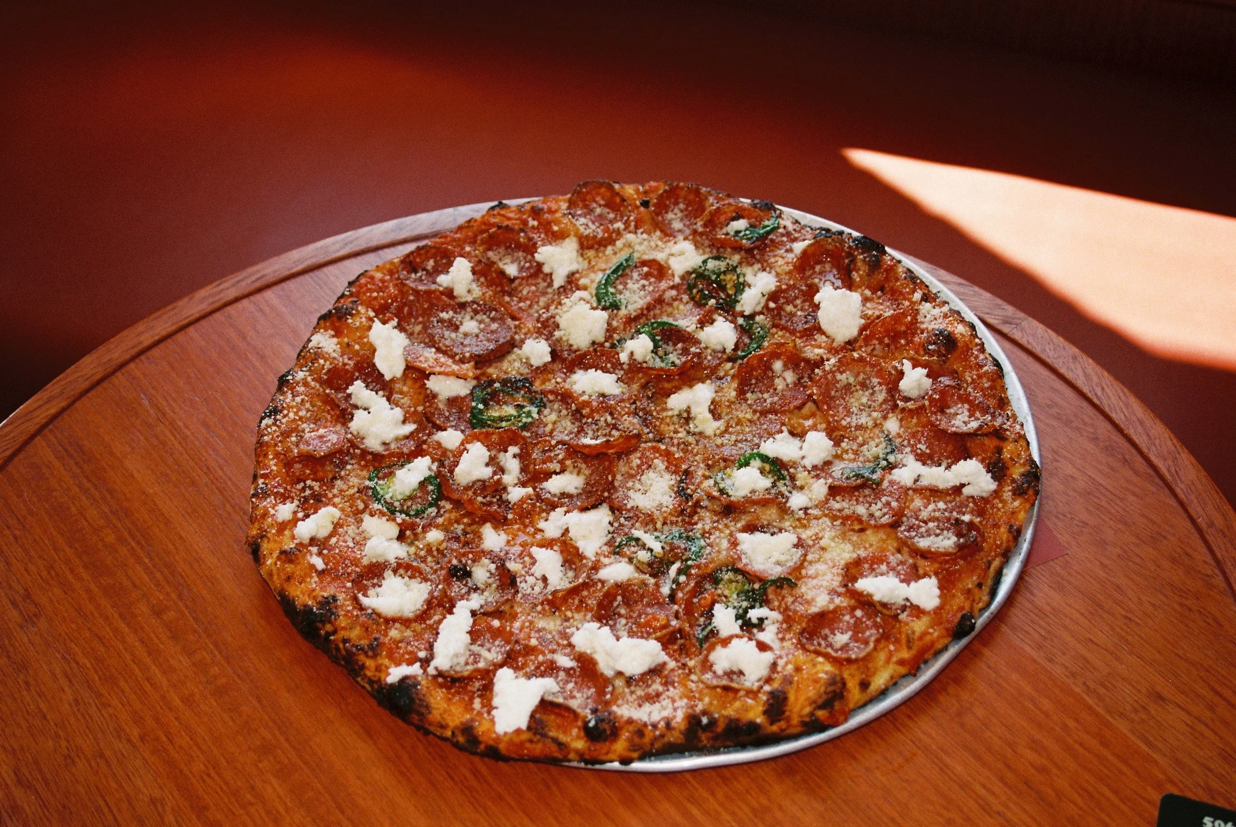 A pizza with pepperoni, green peppers, and cheese on a wooden table.  Club Rose Bay Photography