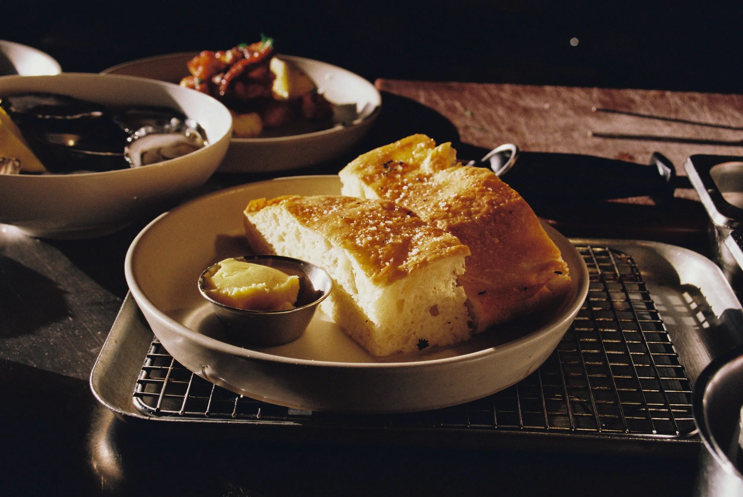 Slices of bread with butter on a white plate, served on a metal rack, with bowls of sauces and toppings in the background. moustache mermaid beach photography