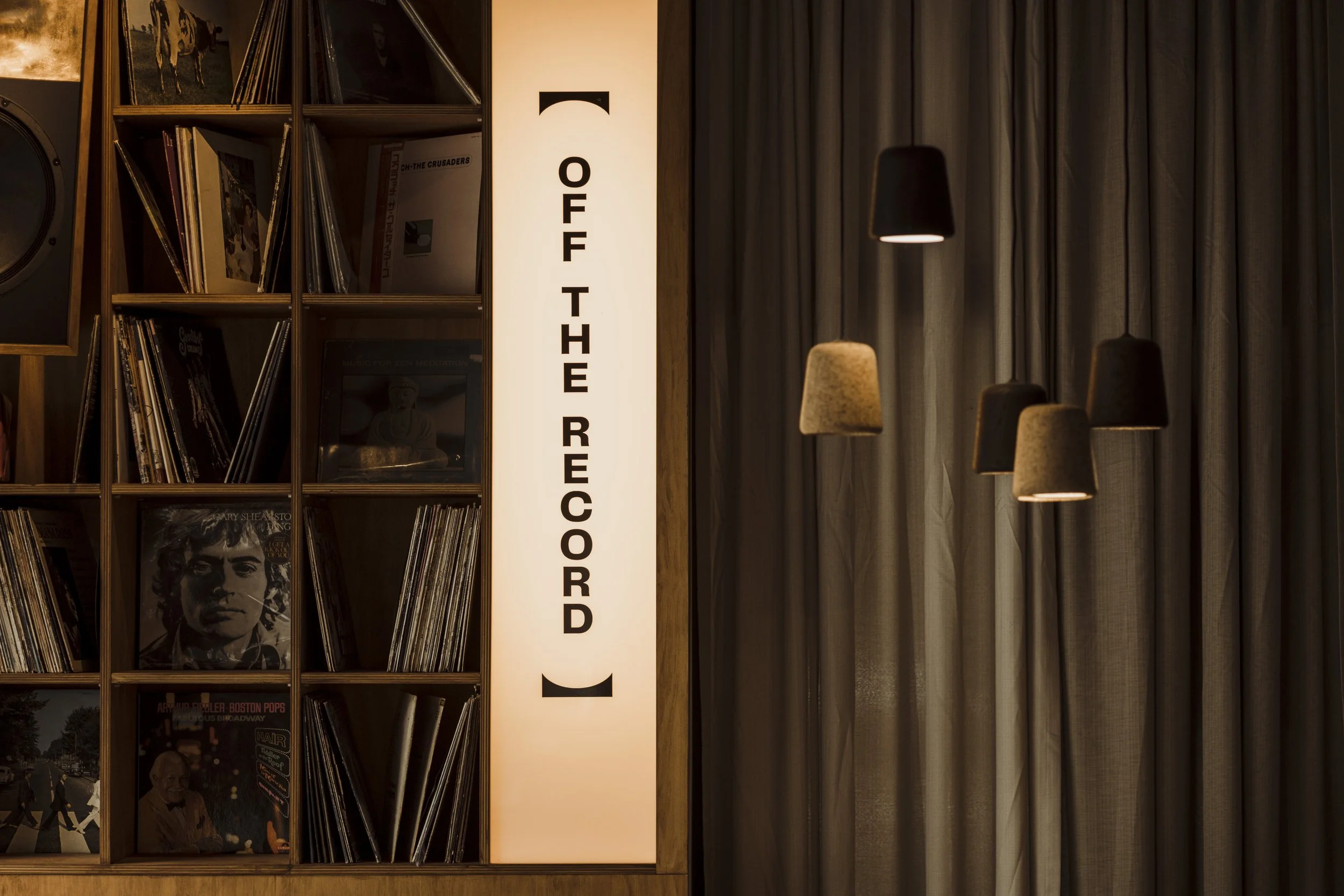 Vinyl records and illuminated "Off the Record" sign with pendant lights.