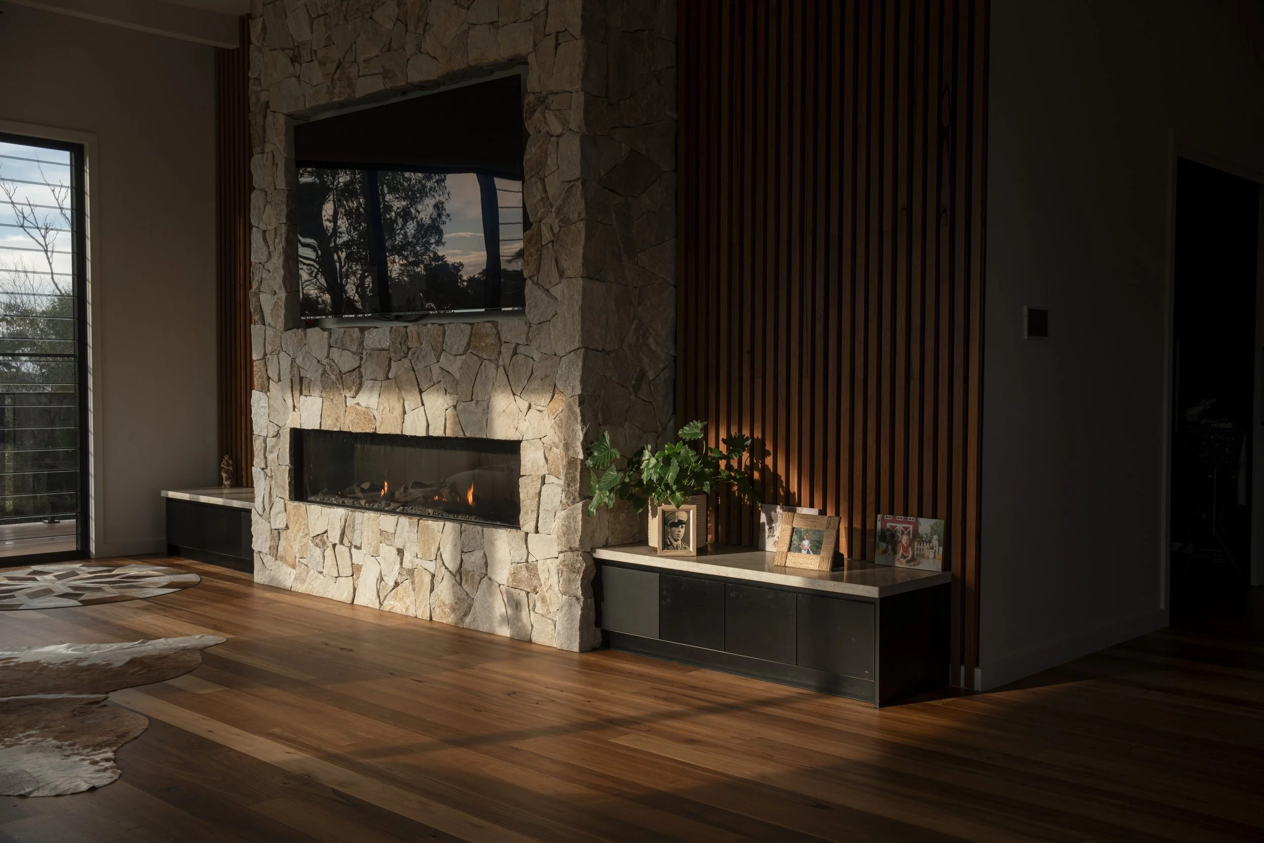 Living room with a stone fireplace. Wooden floor with cowhide rug and sliding glass door to the left. Architecture photography by Joey Bailey Gold Coast