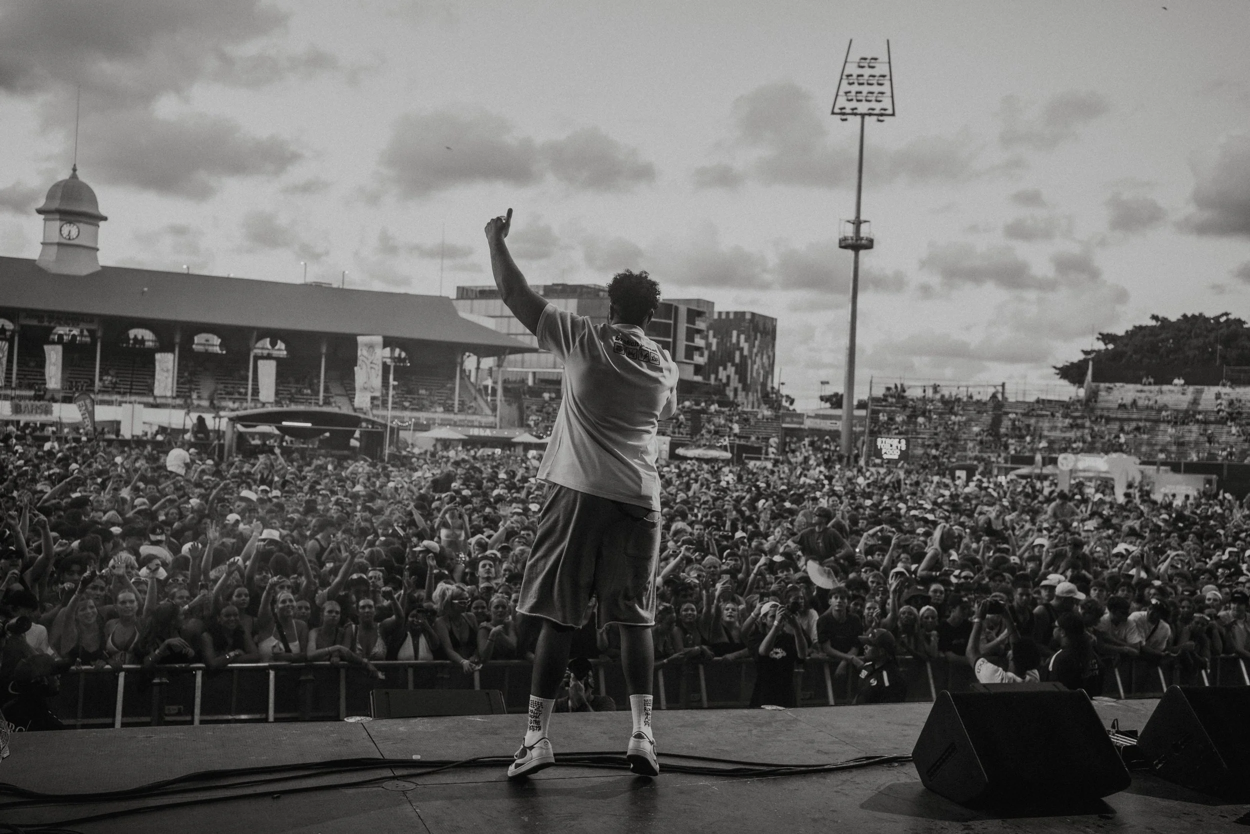 Aj Tracey on stage at a large outdoor music festival with an audience crowding the foreground, black and white photo.
